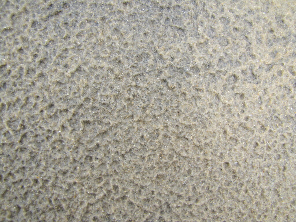 Photograph of sand pockmarked by water.