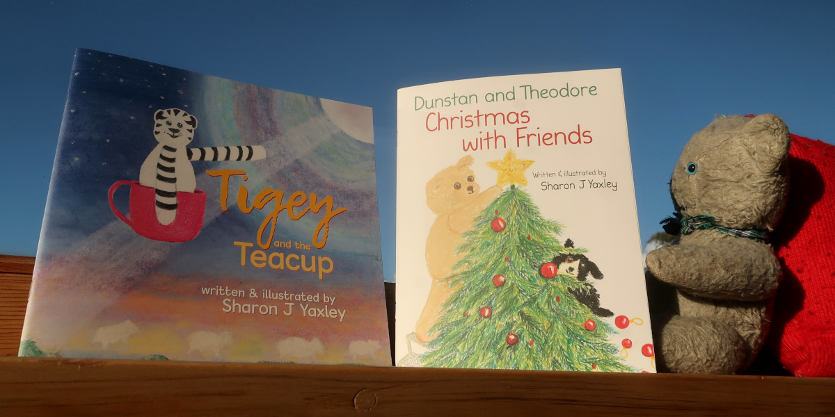 Softcover books titled "Tigey and the Teacup" and "Dunstan and Theodore Christmas with Friends," with a grey teddy bear reading the second book.